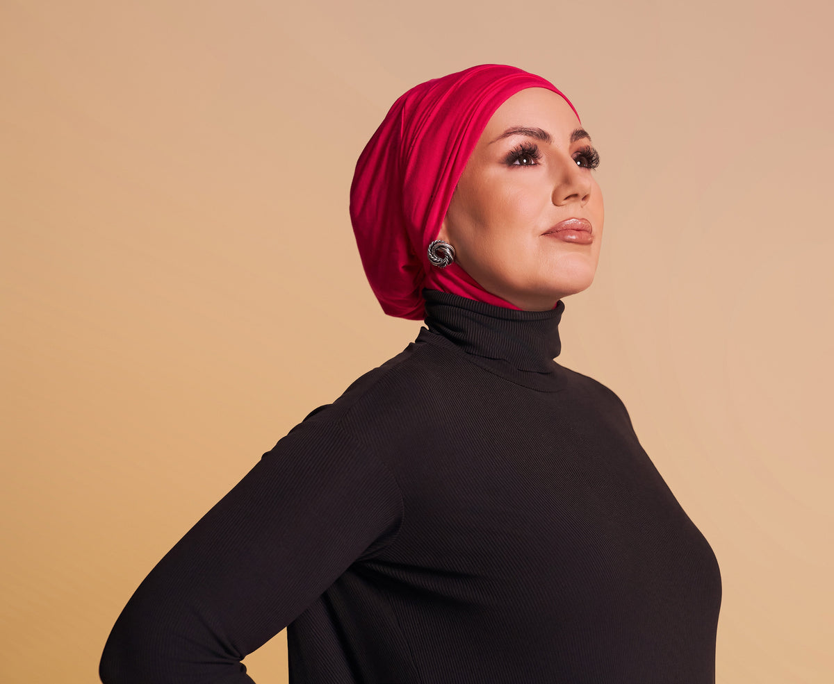 Woman wearing a red hijab and black turtleneck against a beige background