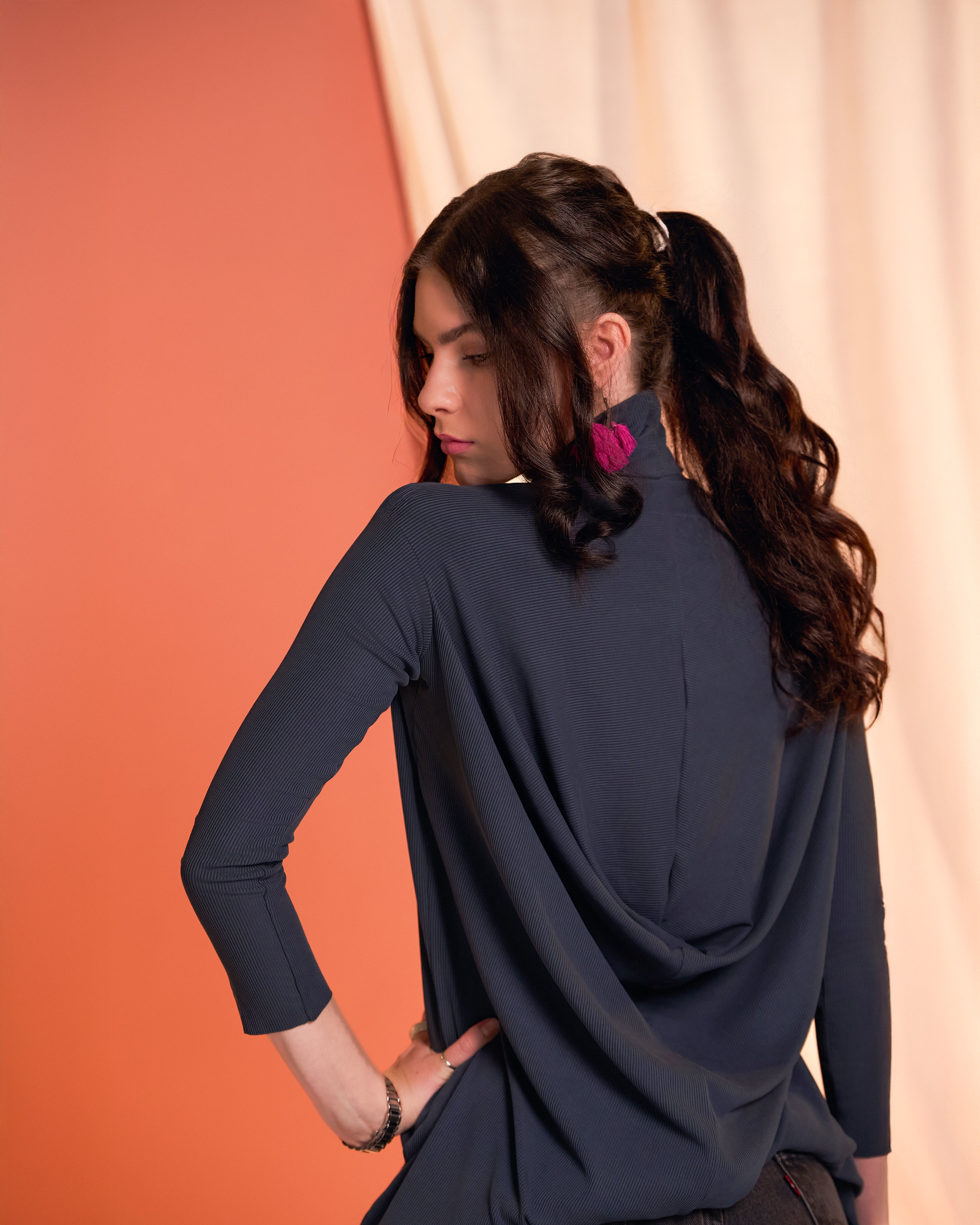 Back view of a woman wearing the Flow Tunic in charcoal. showing the draped back detail in a studio setting.