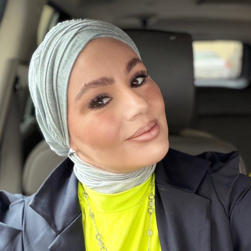 Woman wearing a gray hijab and a bright yellow top inside a vehicle.