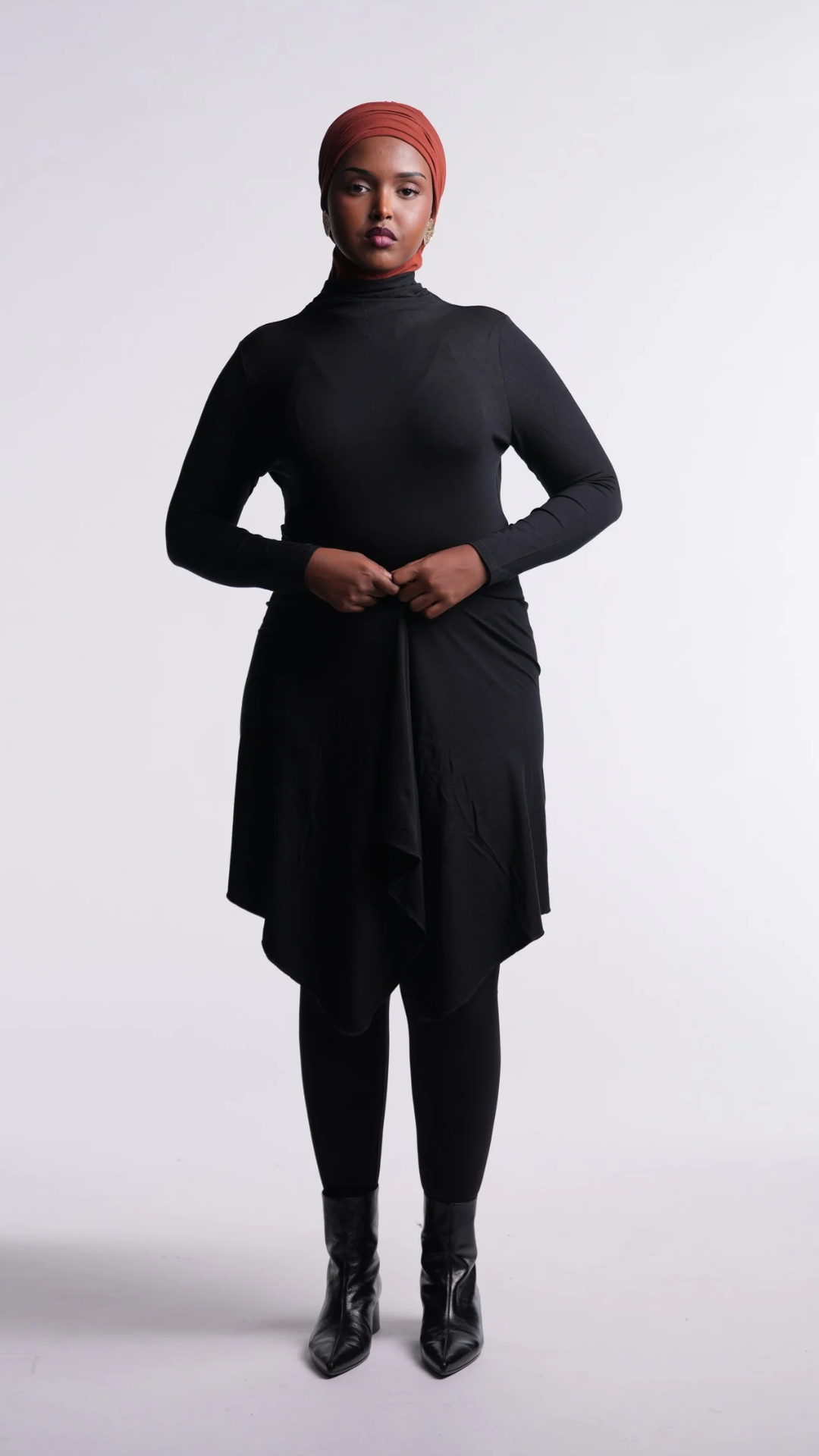 Front view of the Black Convertible Veil Bodysuit with the overlay worn closed, showing the fitted mock-neck bodysuit, styled with black leggings and boots.