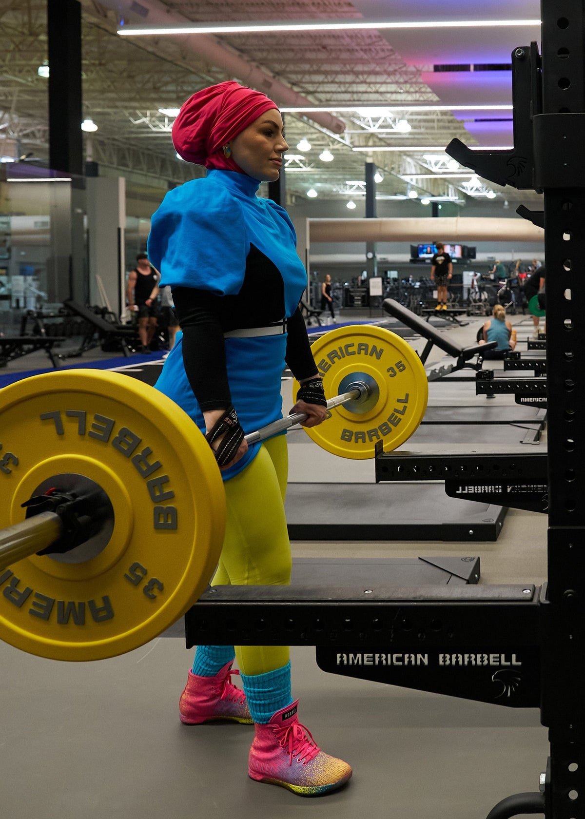 woman with a hijab lifting a barbell with weights in a gym setting