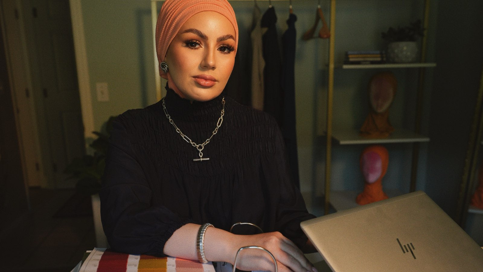 Person wearing a hijab using a laptop at a desk with books and stationery.