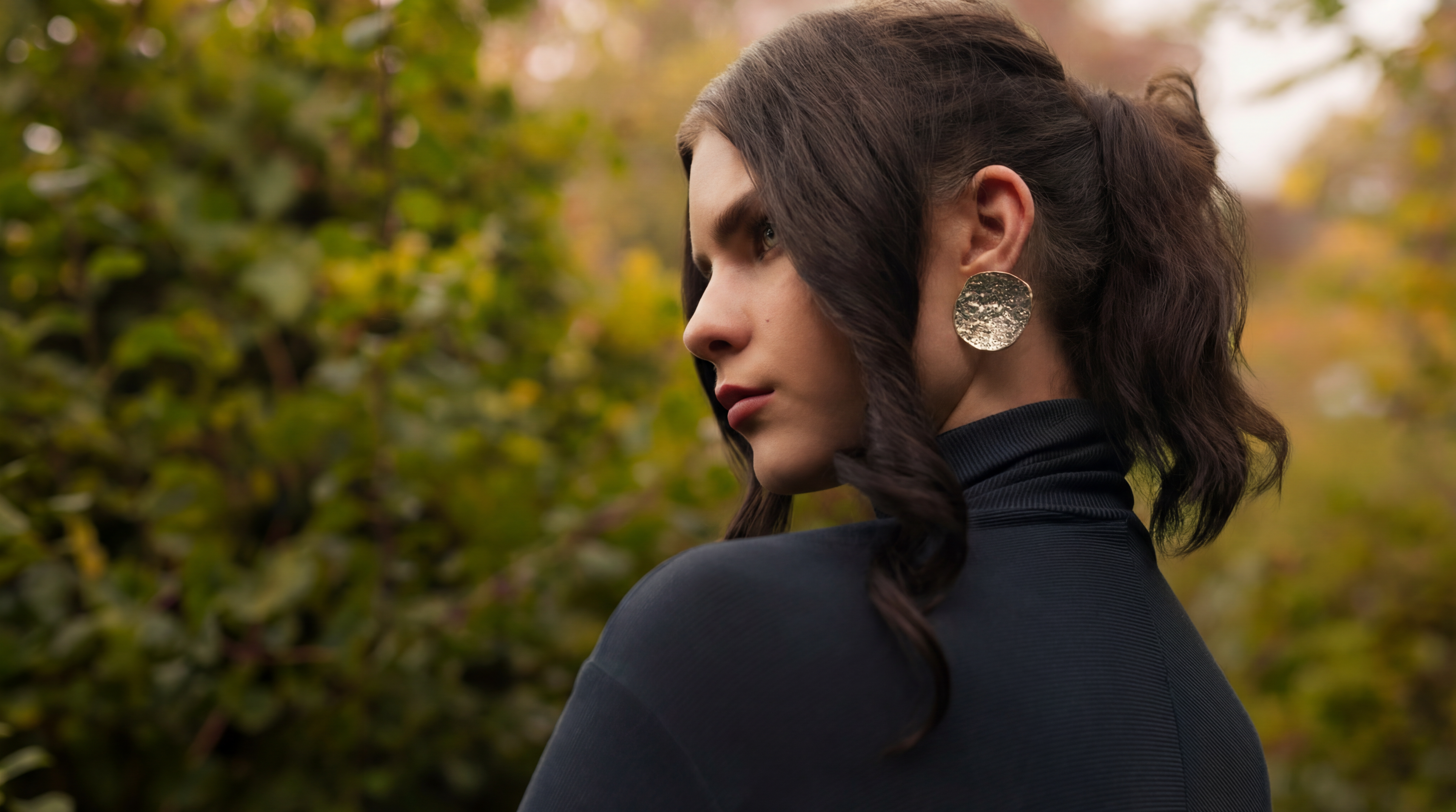 Woman with a ponytail wearing earrings in an outdoor setting