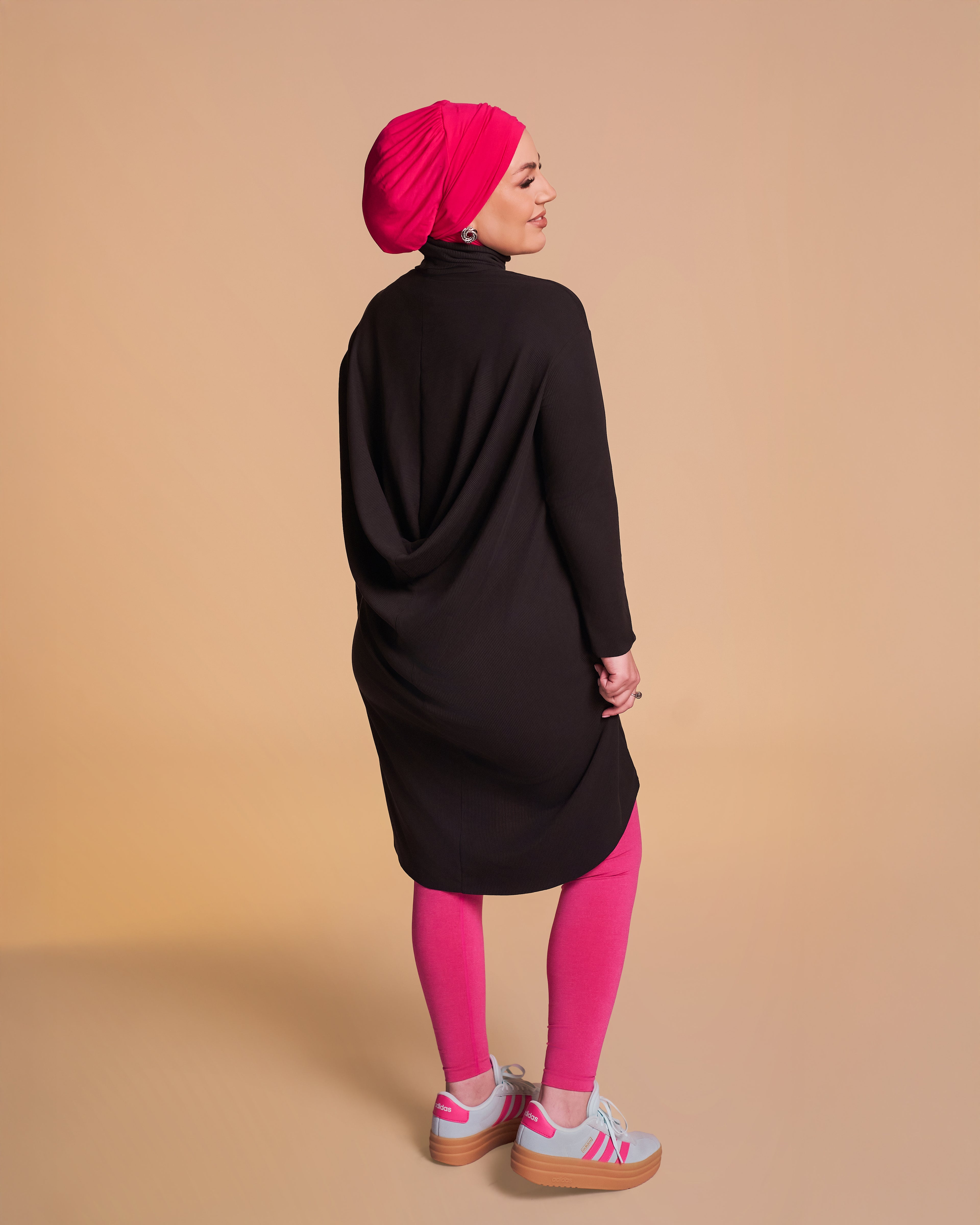 Model is wearing and showing the back view of the DuoWear 2-in-1 Hijab in Hot Pink with Yalla Flow tunic in black. 