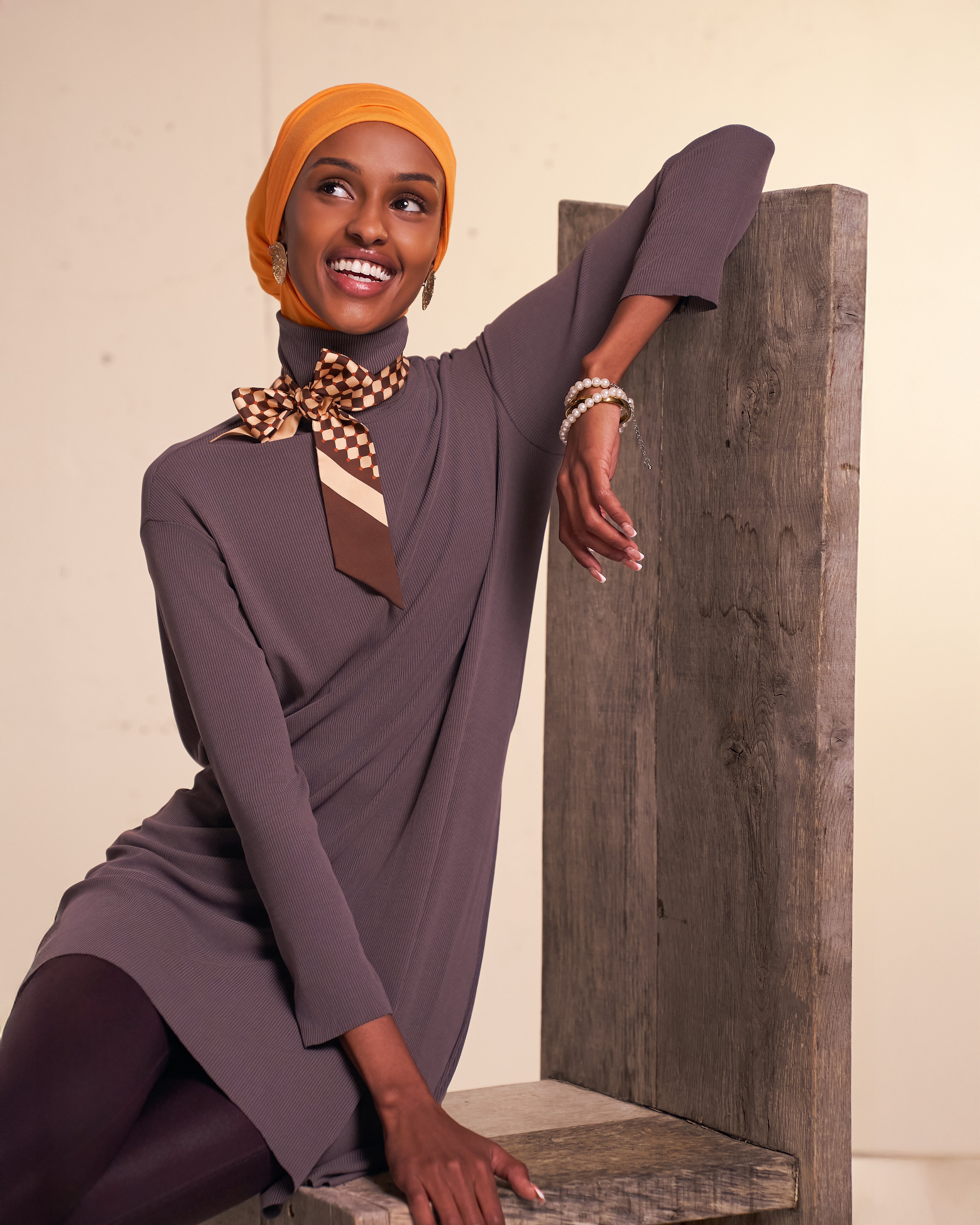Model wearing the DuoWear Hijab with a full-coverage look in Sunburst, seated in a studio setting.