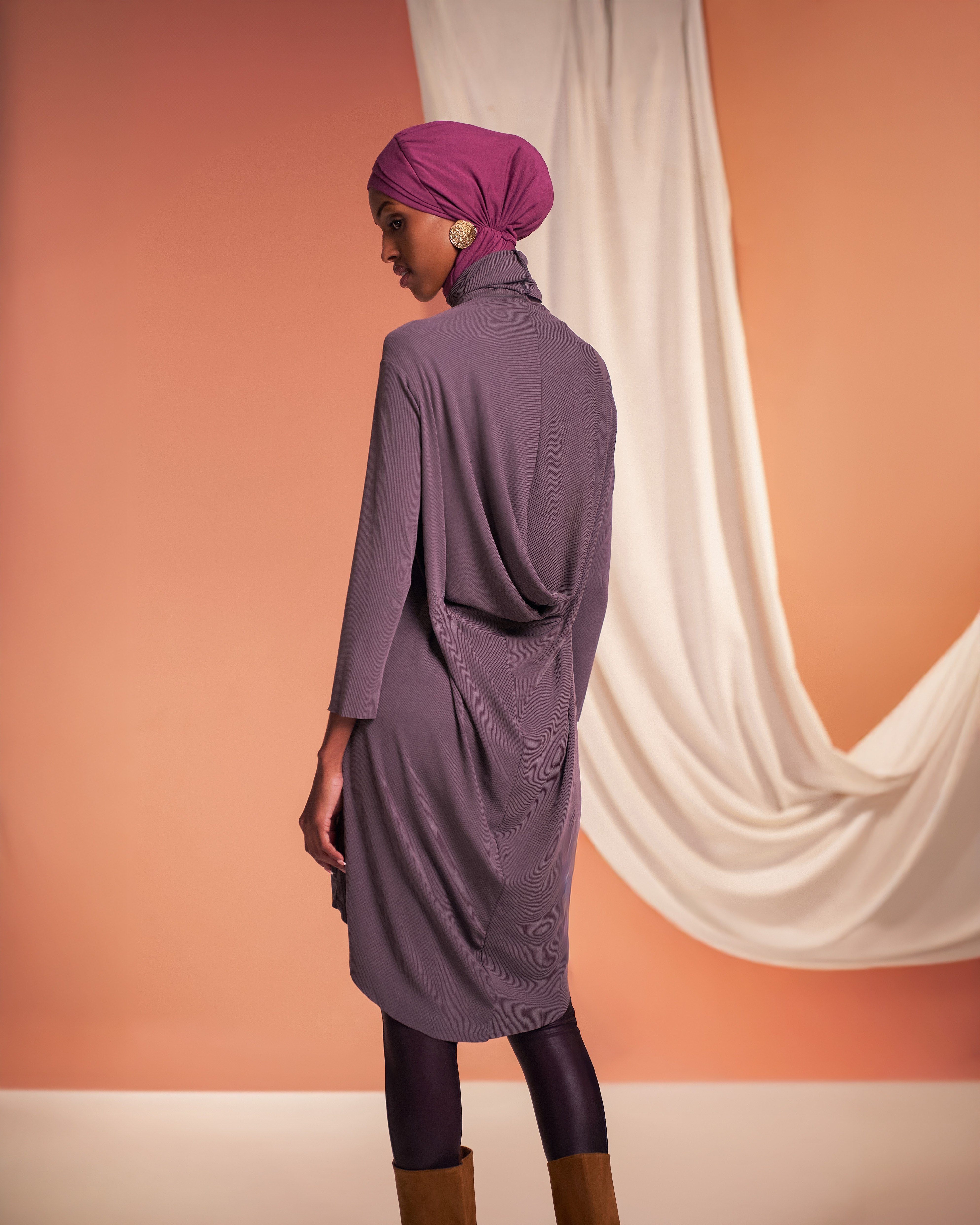 Back view of a woman wearing the DuoSnap Hijab in a magenta tone styled with a Yalla Flow tunic in mink in a studio setting.