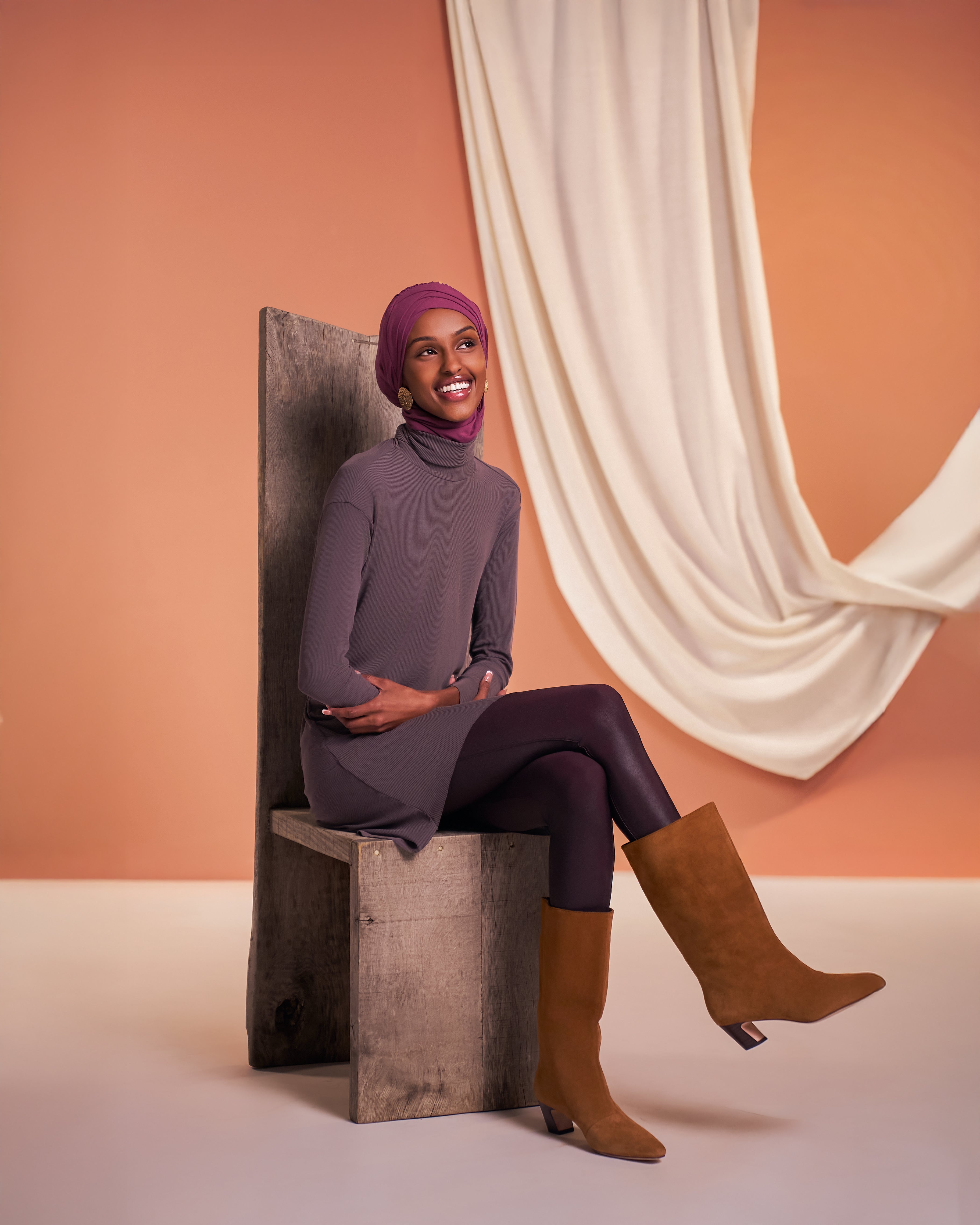 Woman wearing the DuoSnap Hijab in a magenta shade styled with Yalla Flow tunic in mink, seated on a chair in a studio setting.