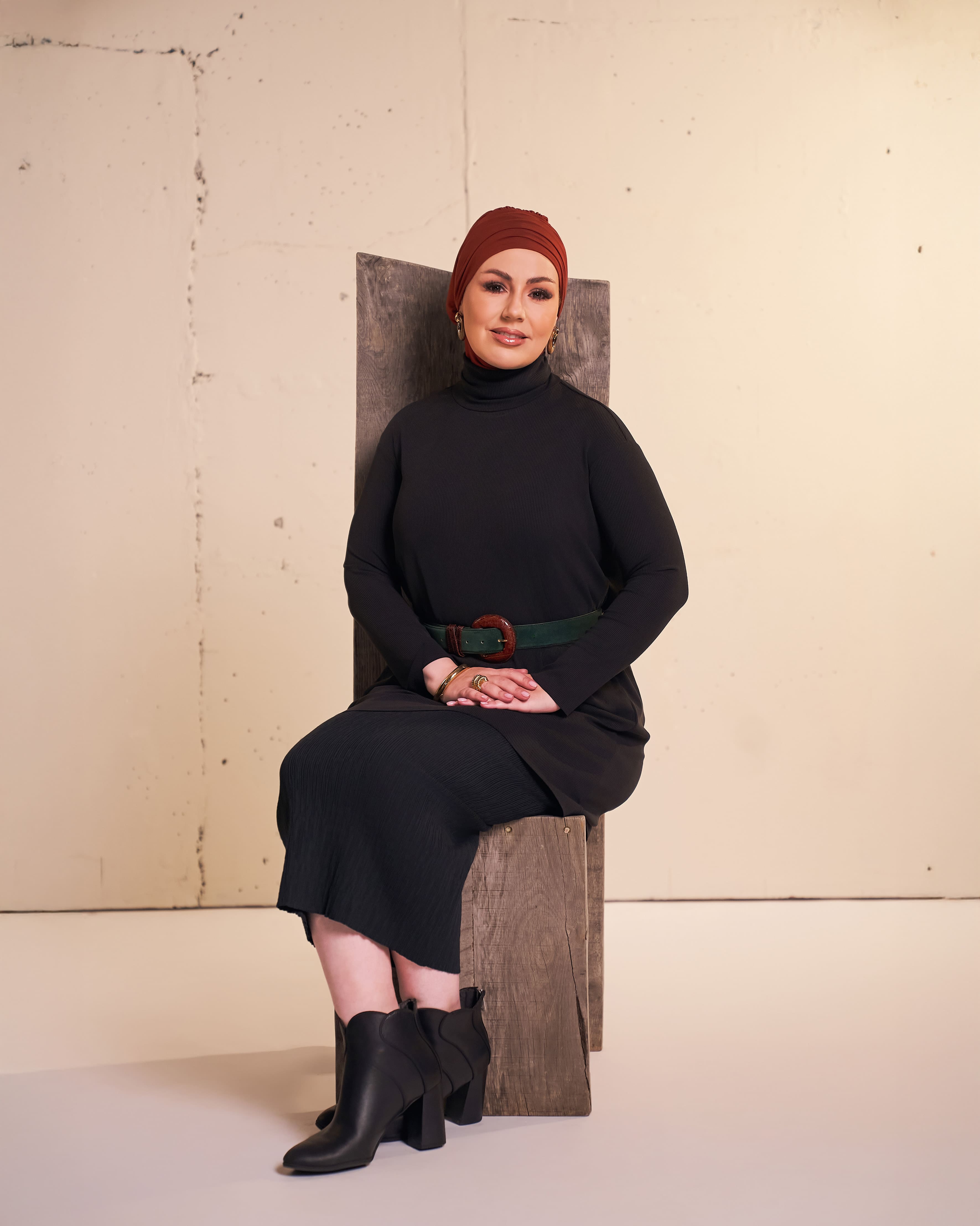 Studio photo of a woman wearing the DuoWear Hijab and the Flow Tunic in black styled with a pencil skirt and ankle boots.