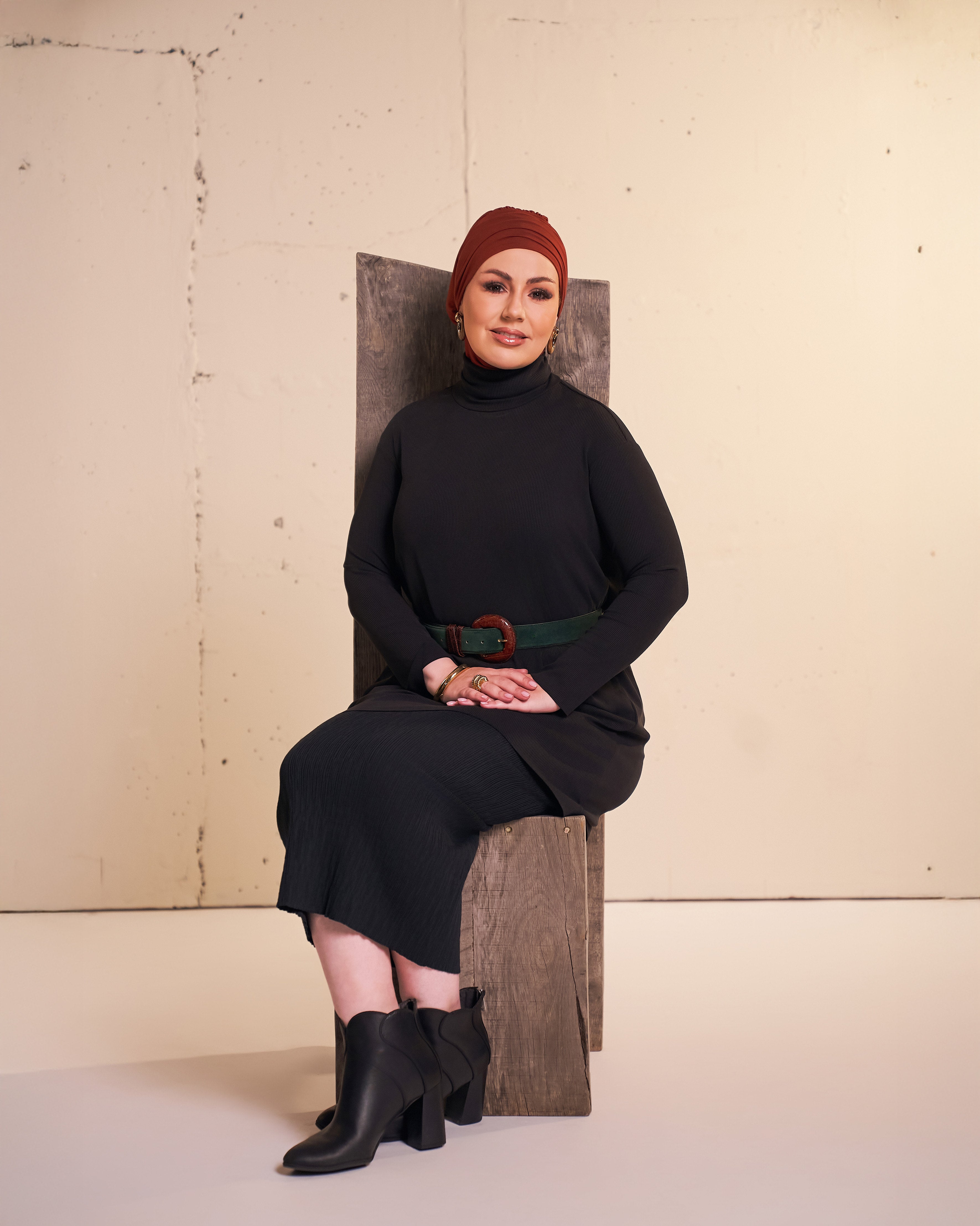 Studio photo of a woman wearing the DuoWear Hijab and the Flow Tunic in black styled with a pencil skirt and ankle boots.