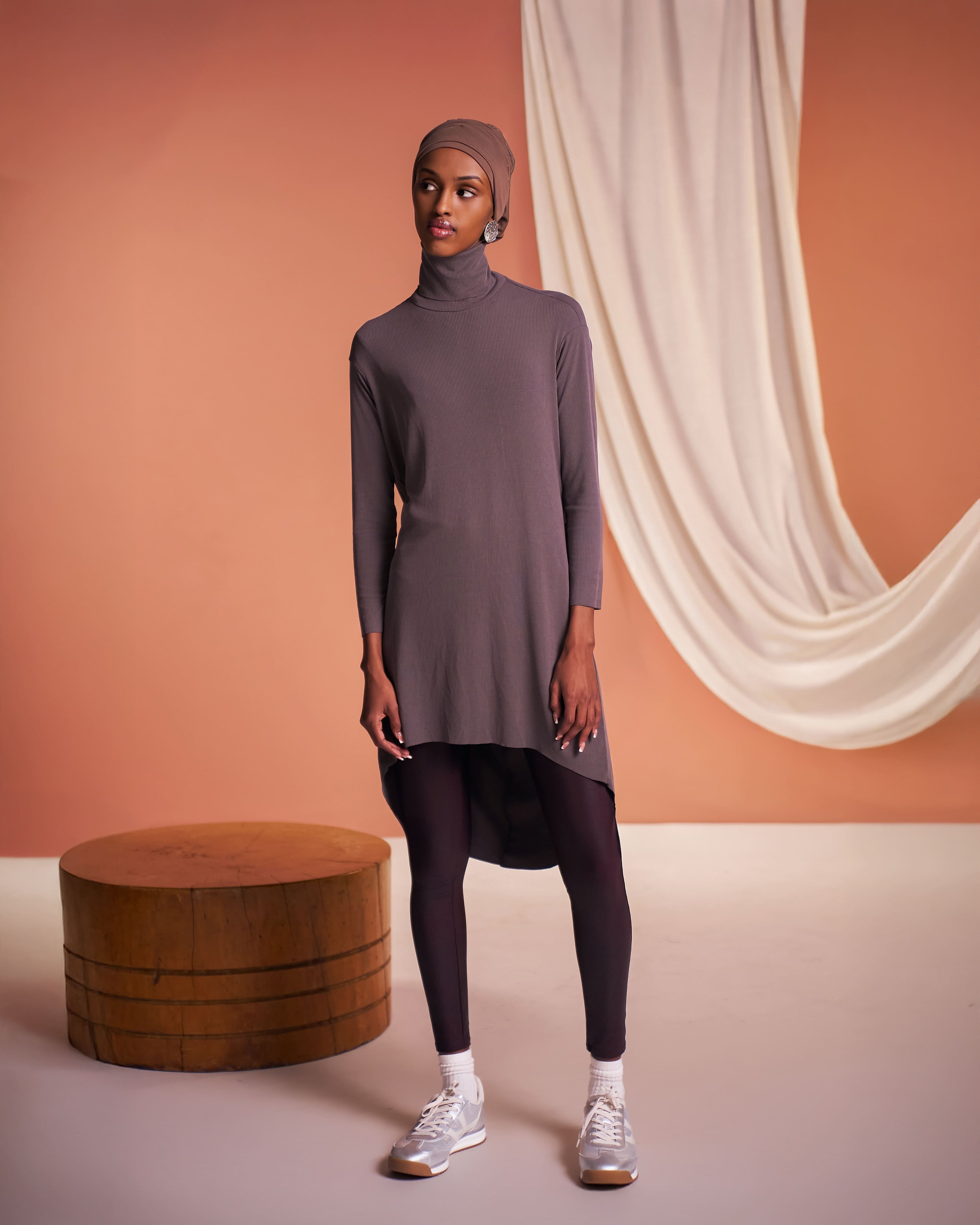 Studio image of a woman wearing the Flow Tunic in mink styled with the DuoWear Hijab and faux leather leggings.