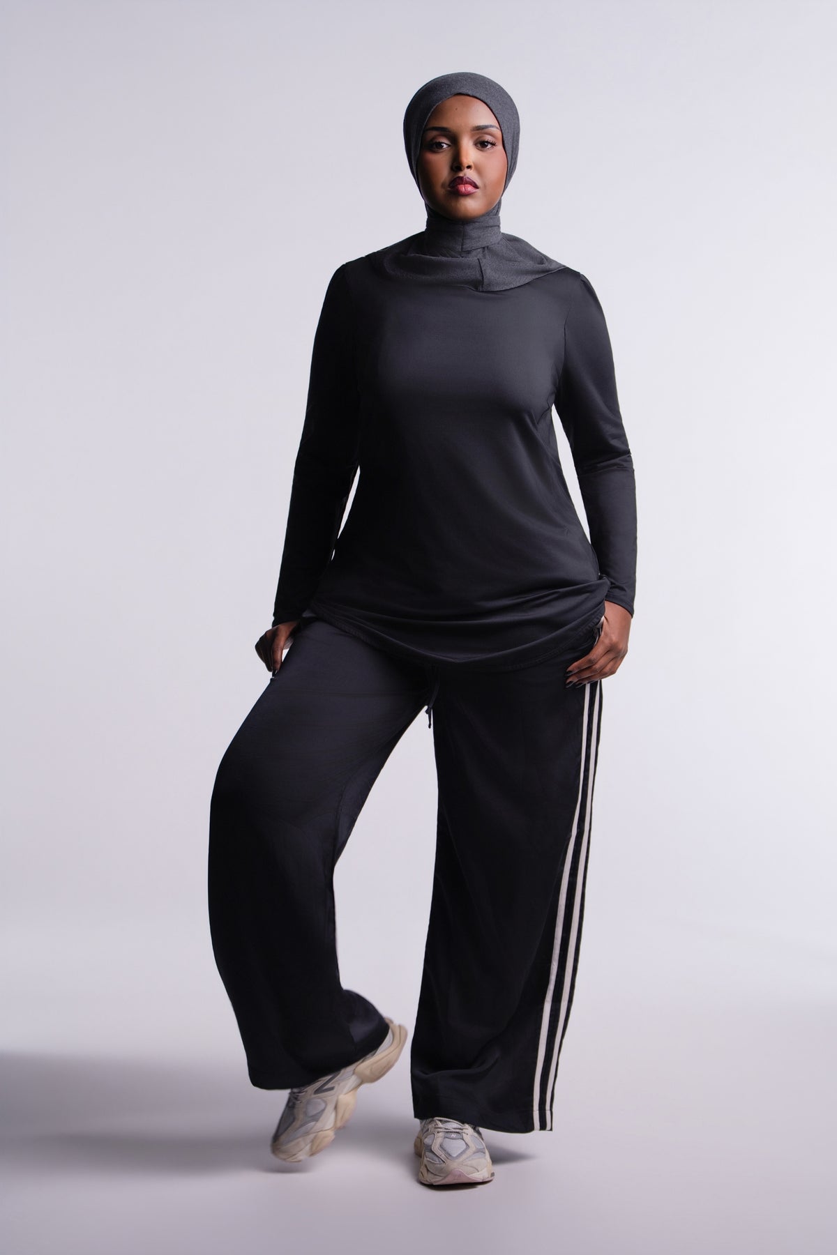 Limitless Top front view, mock neck and tunic length, worn with a gray hijab, black track pants and sneakers