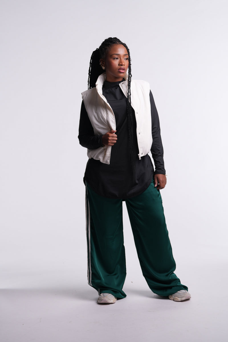 Limitless Top layered under a cream puffer vest, worn with green track pants and sneakers