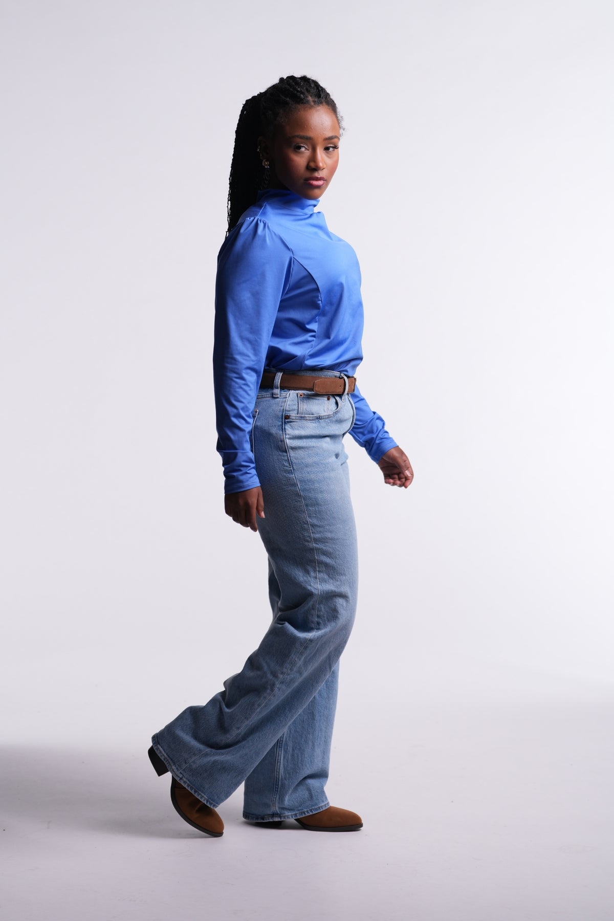 Periwinkle | Limitless Top in periwinkle blue, side view with ruched shoulder, tucked into light-wash jeans with a brown belt and boots