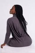 Mink | Model seated in the Flow Tunic, back view, showing the draped back and fitted sleeves.