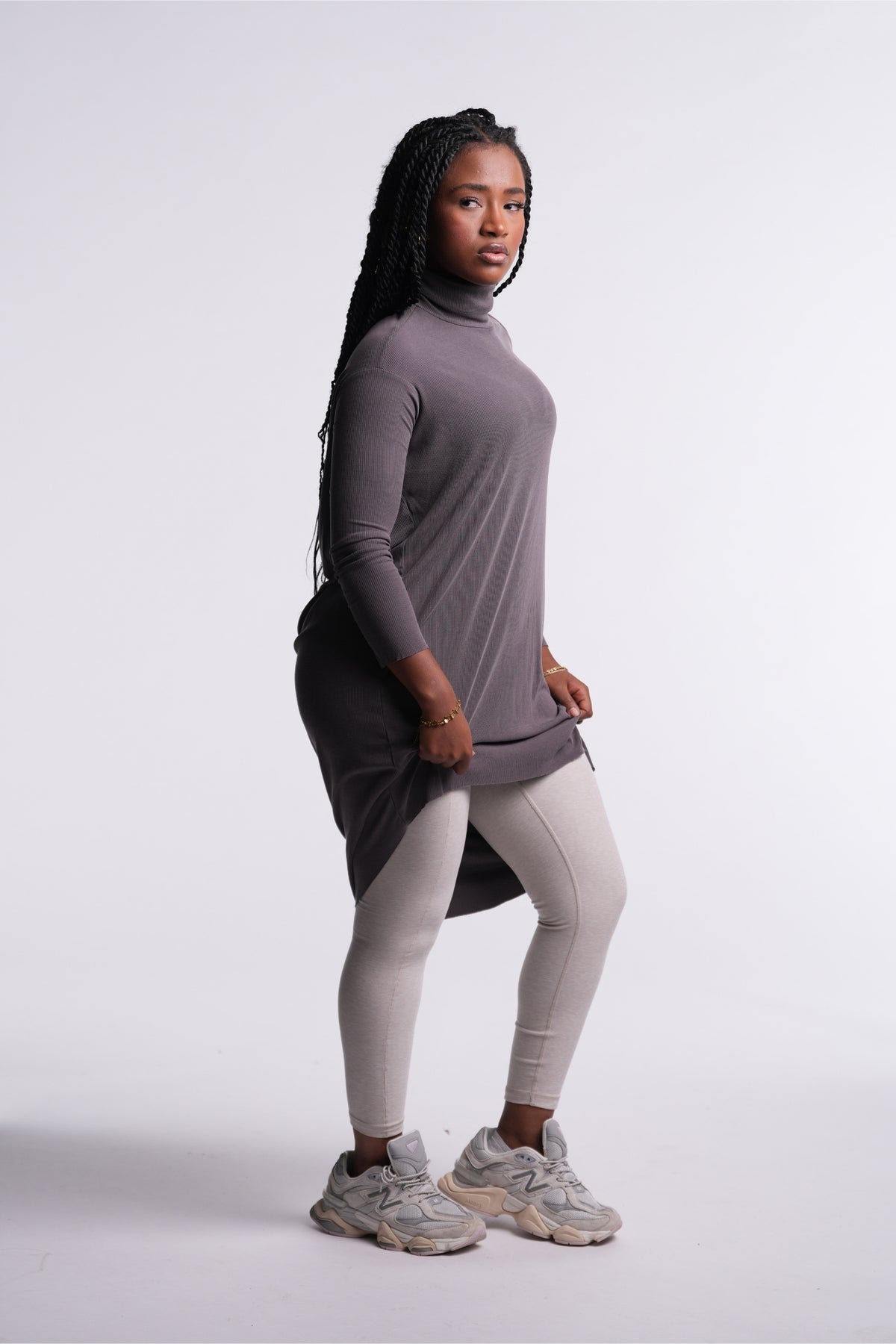 Model in the Mink Flow Tunic with light gray leggings and sneakers, three-quarter view, lifting the hem to show the high-low shape.