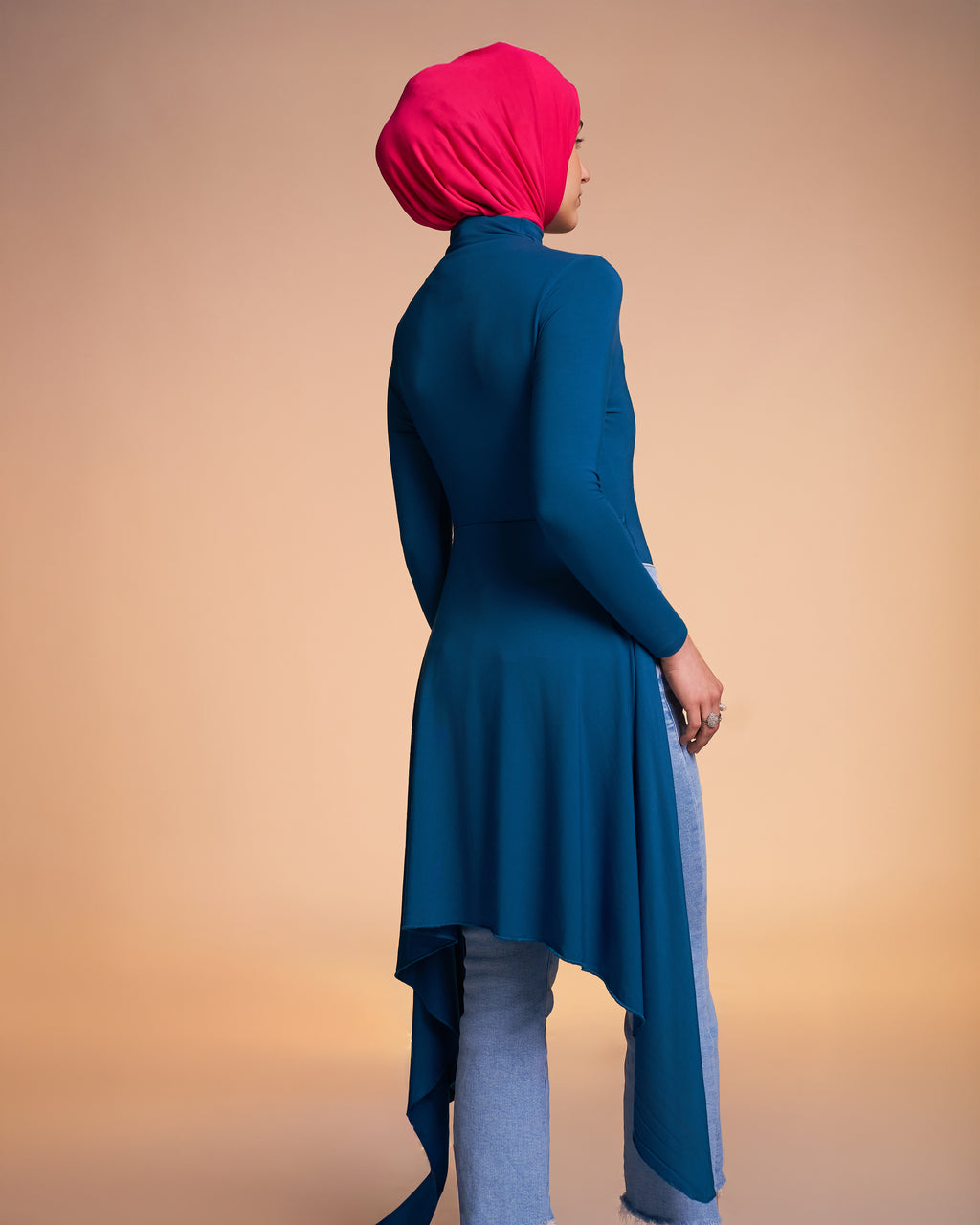 Woman wearing the Veil Bodysuit in teal shows the back view of the tunic length overlay. 