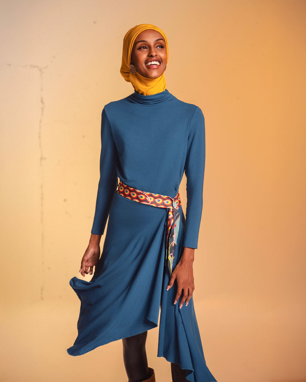 A woman wearing the Veil Bodysuit in teal, with the skirt overlay draped over leggings.