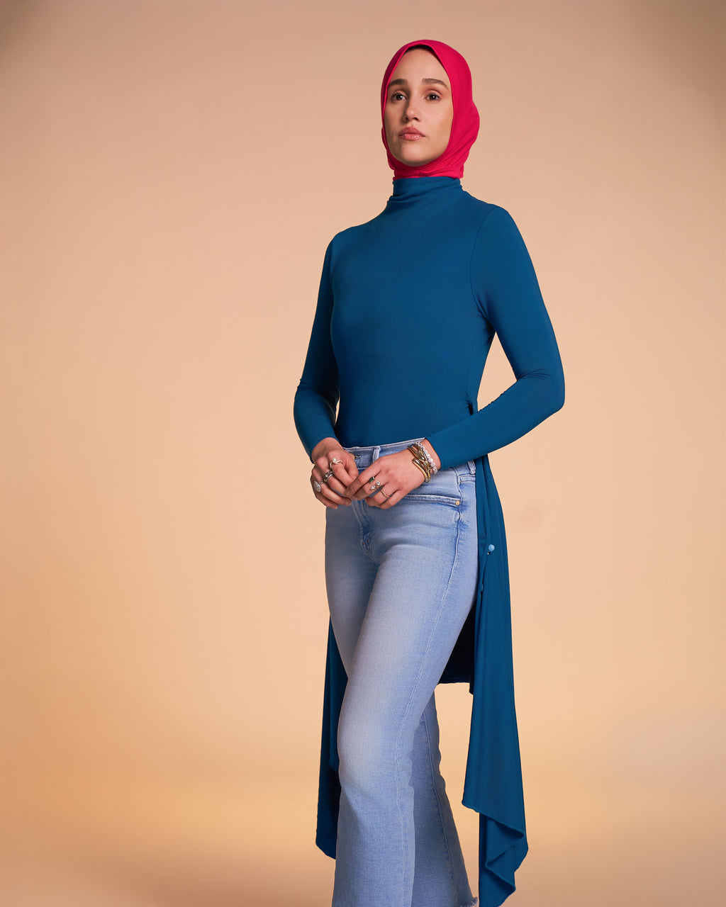 A woman wearing the Veil Bodysuit in teal styled with a pair of denim jeans and the Solo Snap Hijab in hot pink.